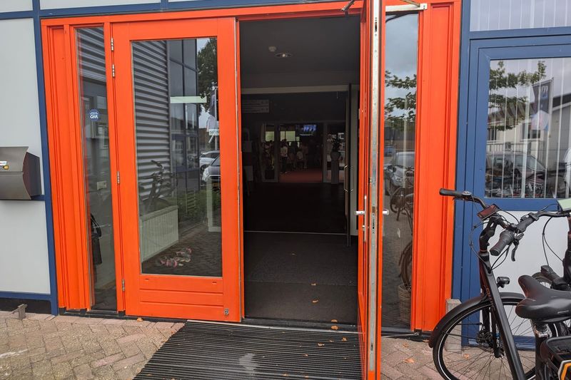 De oranje deuren van Het Lichtbaken staan open. Door de hal zie je de zaal.